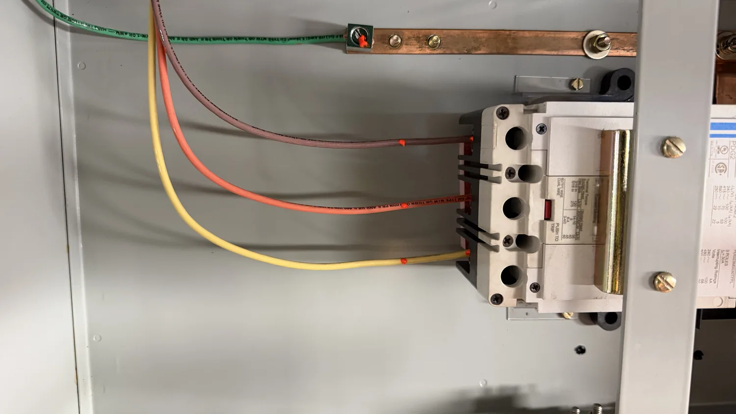 A copper ground bar and contactor inside an enclosure, with yellow, orange and red conductors landed on the terminals