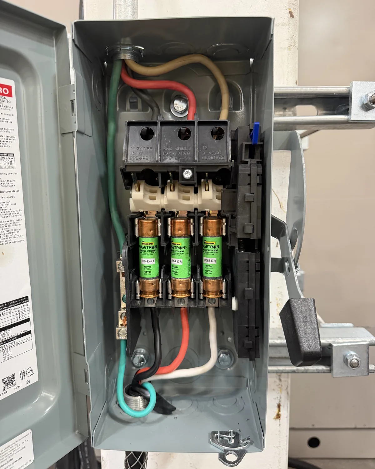 The interior of a fused safety switch with three cartridge fuses and conductors landed on the line and load terminals